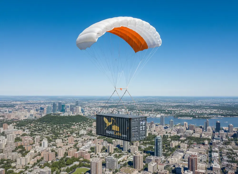 Vue aérienne de Montréal avec un conteneur MobilCube suspendu par un parachute orange et blanc, illustrant la portée de livraison partout au Québec.